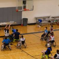Adult in wheelchair shooting a basketball during a basketball game.